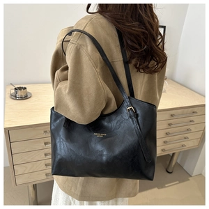 Close-up of a minimalist black leather tote bag with gold lettering shown on a shoulder