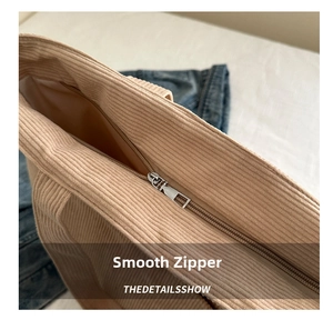 Close-up of smooth metal zipper closure and textured corduroy fabric on a beige tote bag