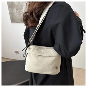 Side view of cream crossbody bag with silver flower logo and wide strap on black coat