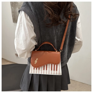 Detail of music-themed crossbody bag featuring piano key pattern and golden treble clef
