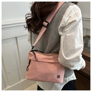 Close-up of pink crossbody bag showing fabric texture, zipper pocket, and silver petal logo