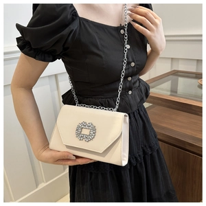 Detail of off-white leather crossbody bag featuring a sparkling crystal buckle and chain
