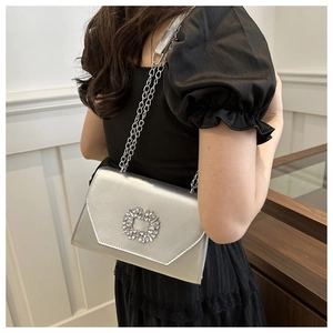 Close-up of a silver chain bag with a sparkling crystal floral buckle and metallic finish