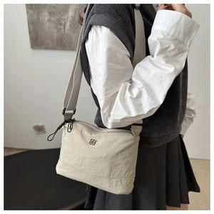 Detail of a beige nylon crossbody bag featuring a flower metal logo and wide knit strap