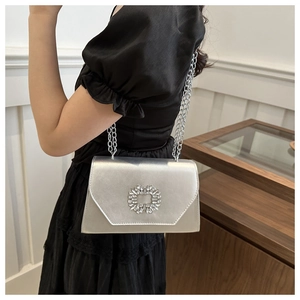 Detail of silver satin evening bag with rhinestone buckle worn over a black dress