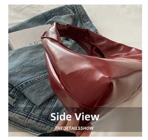 Side view of chic burgundy patent leather crescent bag on aesthetic background