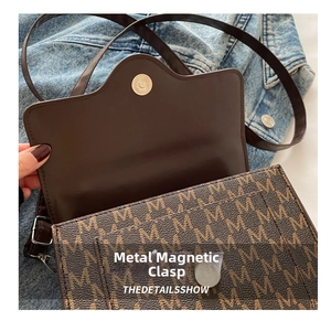 Close-up of the silver magnetic snap closure and M-pattern on dark brown crossbody bag