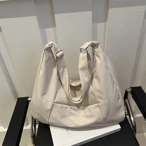 Borsa tote beige minimalista con ampia tracolla su una sedia nera moderna