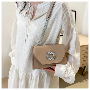 Detail of a beige crossbody bag with a sparkling rhinestone buckle and metal chain strap