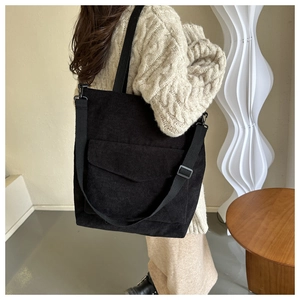 Detailed view of black corduroy tote bag with adjustable strap and front envelope pocket
