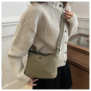 Close-up of olive green nylon crossbody bag featuring a metal floral logo on model