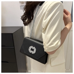 Detail of black crossbody bag with rhinestone buckle and silver chain on cream blazer