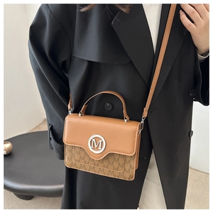 Detail of light brown crossbody bag featuring silver M buckle and monogram print overlay