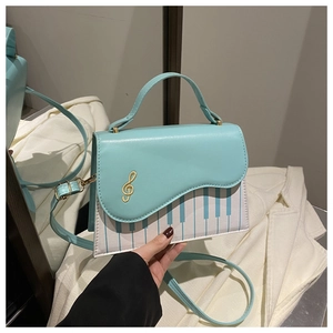 Detail of mint green handbag featuring piano key pattern and gold clef embroidery detail