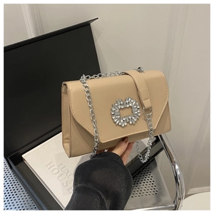 Detail of beige leather crossbody bag with a large sparkling crystal buckle and silver chain