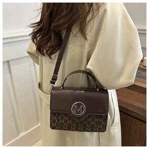Detail of dark brown handbag showing M-logo buckle, monogram print, and shoulder strap