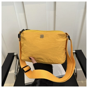 Detail of yellow nylon crossbody bag featuring silver flower logo and adjustable strap