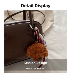 Detail of a brown leather handbag with embossed letters and a fuzzy teddy bear charm