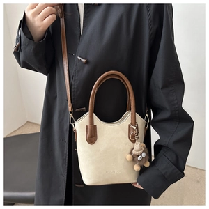 Dettaglio borsa a secchiello in pelle scamosciata beige e marrone con ciondolo peluche