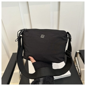 Detail of black nylon crossbody bag featuring silver floral logo and wide fabric strap