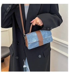 Detail of blue denim crossbody bag with brown leather straps worn with a black blazer