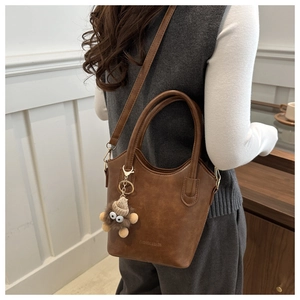 Detail of brown vintage PU leather bucket bag with plush charm and embossed lettering