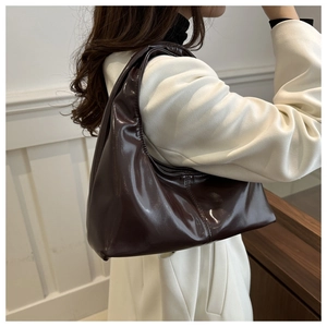 Detailed view of coffee brown patent leather shoulder bag worn by model in a minimalist setting