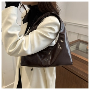 Gros plan d'un sac hobo en cuir verni marron foncé brillant porté avec un blazer blanc