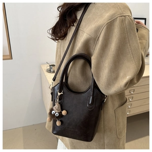 Close-up of a brown leather bucket bag with a fuzzy monster charm and top handles