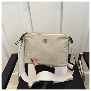 Macro view of beige nylon crossbody bag featuring textured fabric and metal logo detail