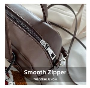 Detail view of smooth silver metal zipper and fine stitching on dark brown leather bag