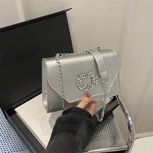 Silver metallic crossbody bag with rhinestone buckle and chain strap shown on black box