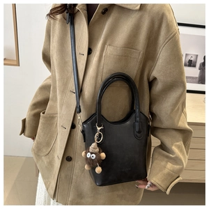 Detail of black leather handbag with a plush monster charm and fashion lettering