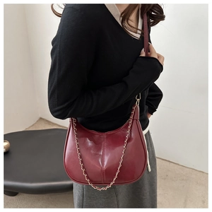 Detail of burgundy hobo bag with glossy leather texture and delicate gold chain strap