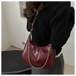Detail of burgundy underarm bag with glossy texture and gold chain decoration