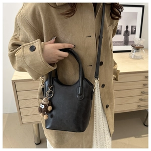 Close-up of black leather crossbody bag with teddy bear charm and fashion text