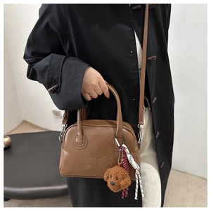 Close-up of brown textured handbag with letter embossing and plush puppy pendant accessory