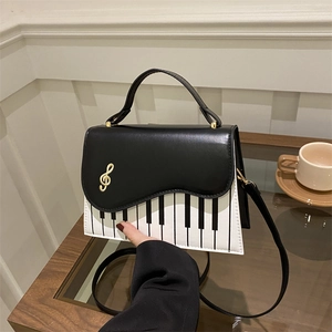Square crossbody bag with piano key print and golden musical note charm on white wood