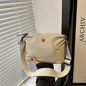 Minimalist beige nylon tote bag with wide shoulder strap and clover logo in natural light