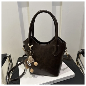 Detail of dark brown vintage PU bucket bag with leather texture and cute plush pendant