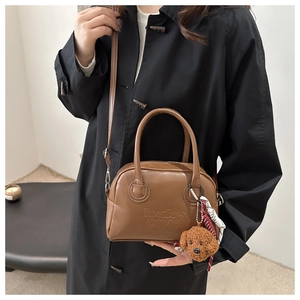 Detail of a brown vintage Boston bag with plush bear charm and woven keychain