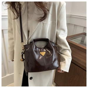 Detalle de bolso de charol brillante marrón oscuro con herrajes dorados y un colgante
