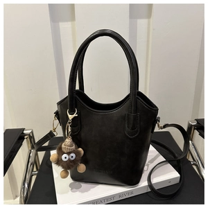 Detail of black faux leather bucket bag with plush charm and fashion text print