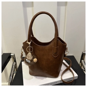 Detail of dark brown vintage PU leather bucket bag with plush charm on white books