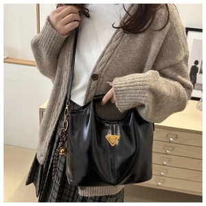 Detalle de bolso en piel sintética negra brillante con logo metálico dorado y asa