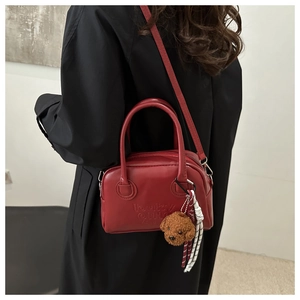 Detail view of red leather handbag featuring embossed lettering and plush bear charm