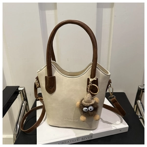 Detail of cream bucket bag with brown handles, adjustable strap and plush bear charm