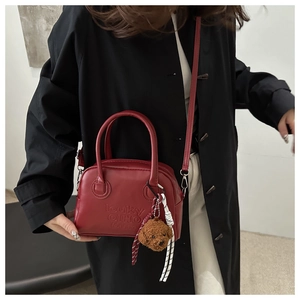 Detail of red synthetic leather pillow bag with plush dog charm and crossbody strap
