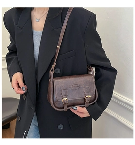 Detailed view of brown vintage PU leather messenger bag worn on a black blazer