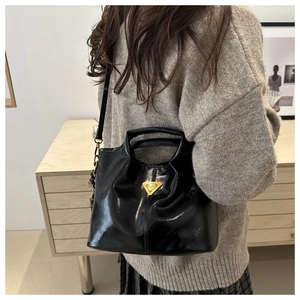Detalle de bolso cubo en charol negro brillante con logo de triángulo dorado y bandolera